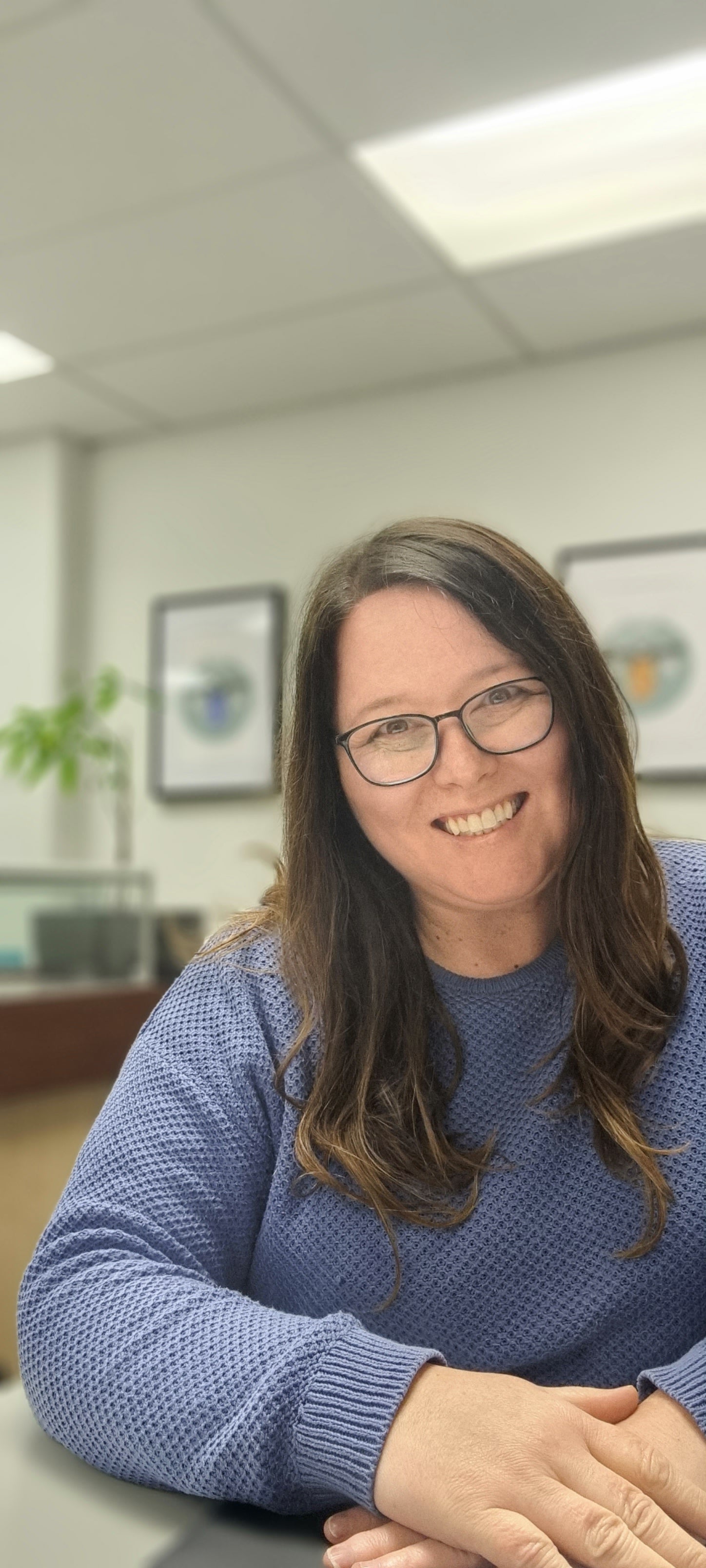 Woman with brown hair wearing a blue jumper and glasses